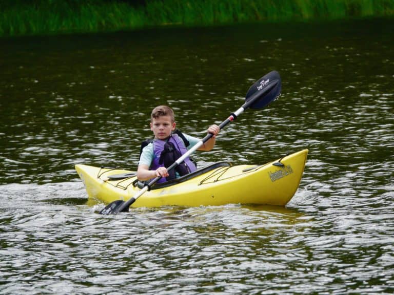 A boy paddles a yellow kayak in a stream
