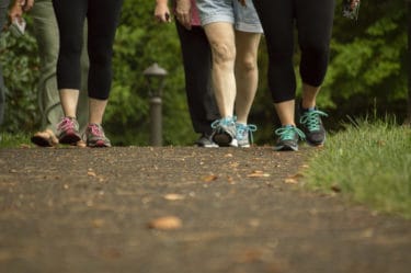 The lower legs and feet of five women wearing sneakers walking on a paved path in daylight