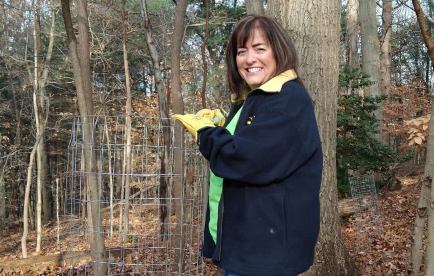 Smiling woman in woods, holding tree cage