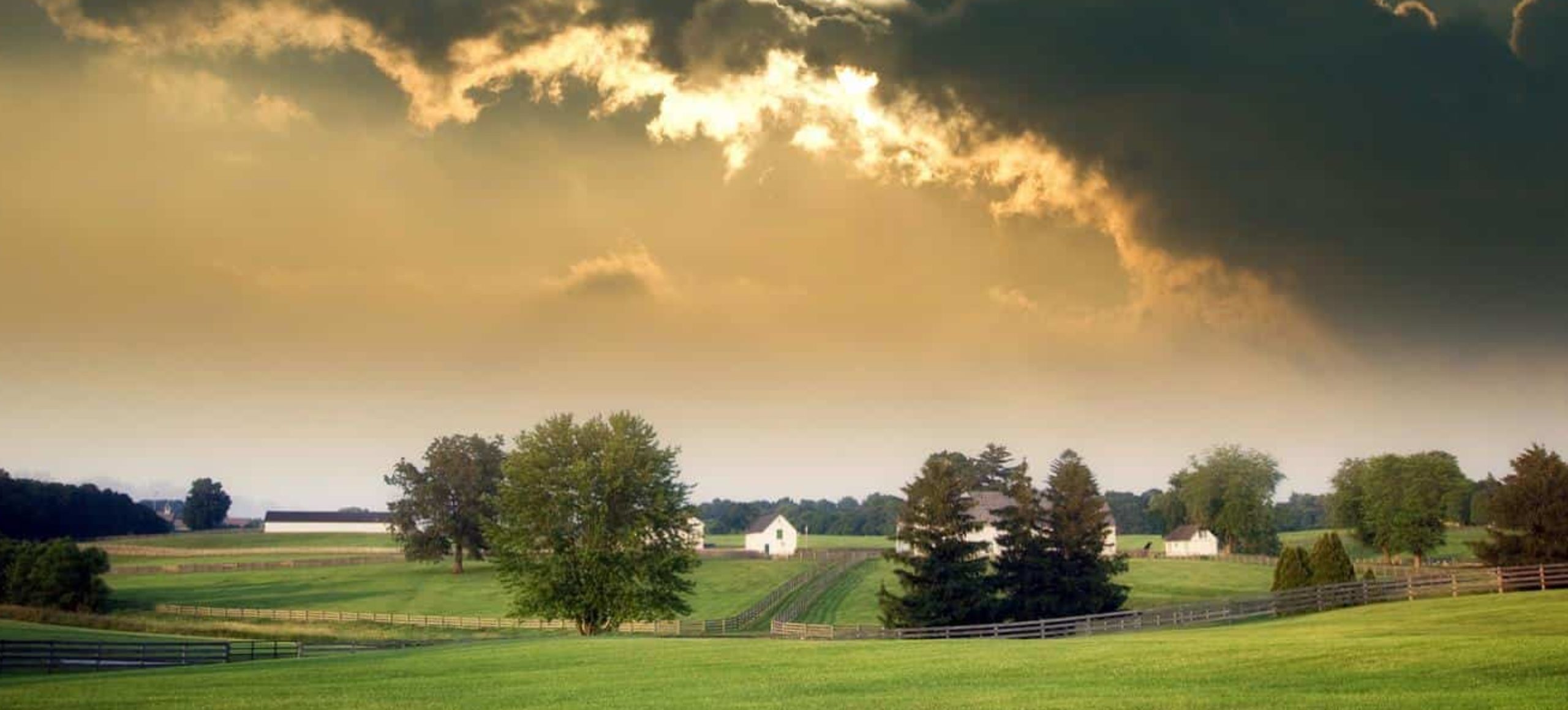 Sunset over a pastoral farm with green fields and farm buildings.