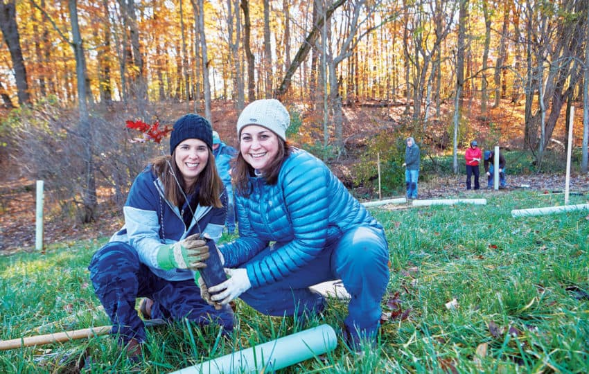 Two women holding a tree seedling outdoors at a tree planting event.