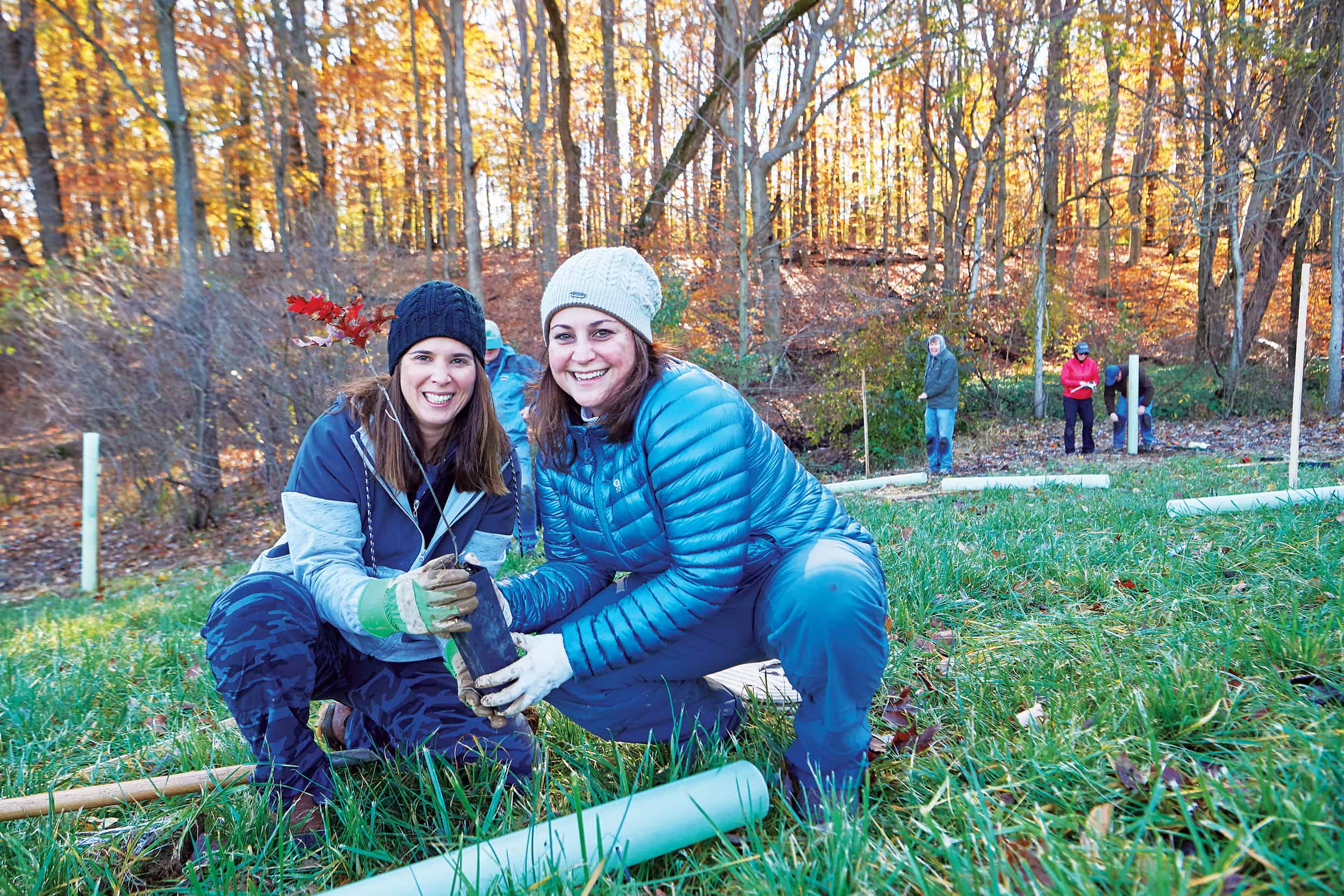 Two women holding a tree seedling outdoors at a tree planting event.