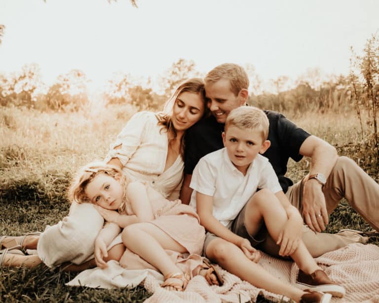 A family sits on a blanket in a natural setting.