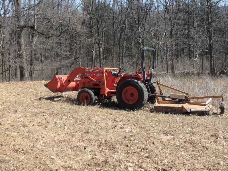 An orange tractor with a brush hog in a meadow.