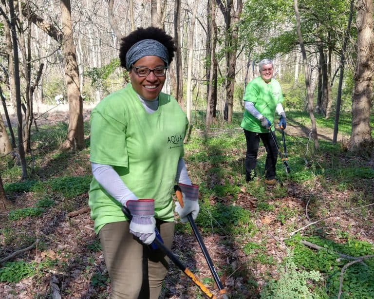 Two women with Aqua company shirts on prune invasive vines in a forest.