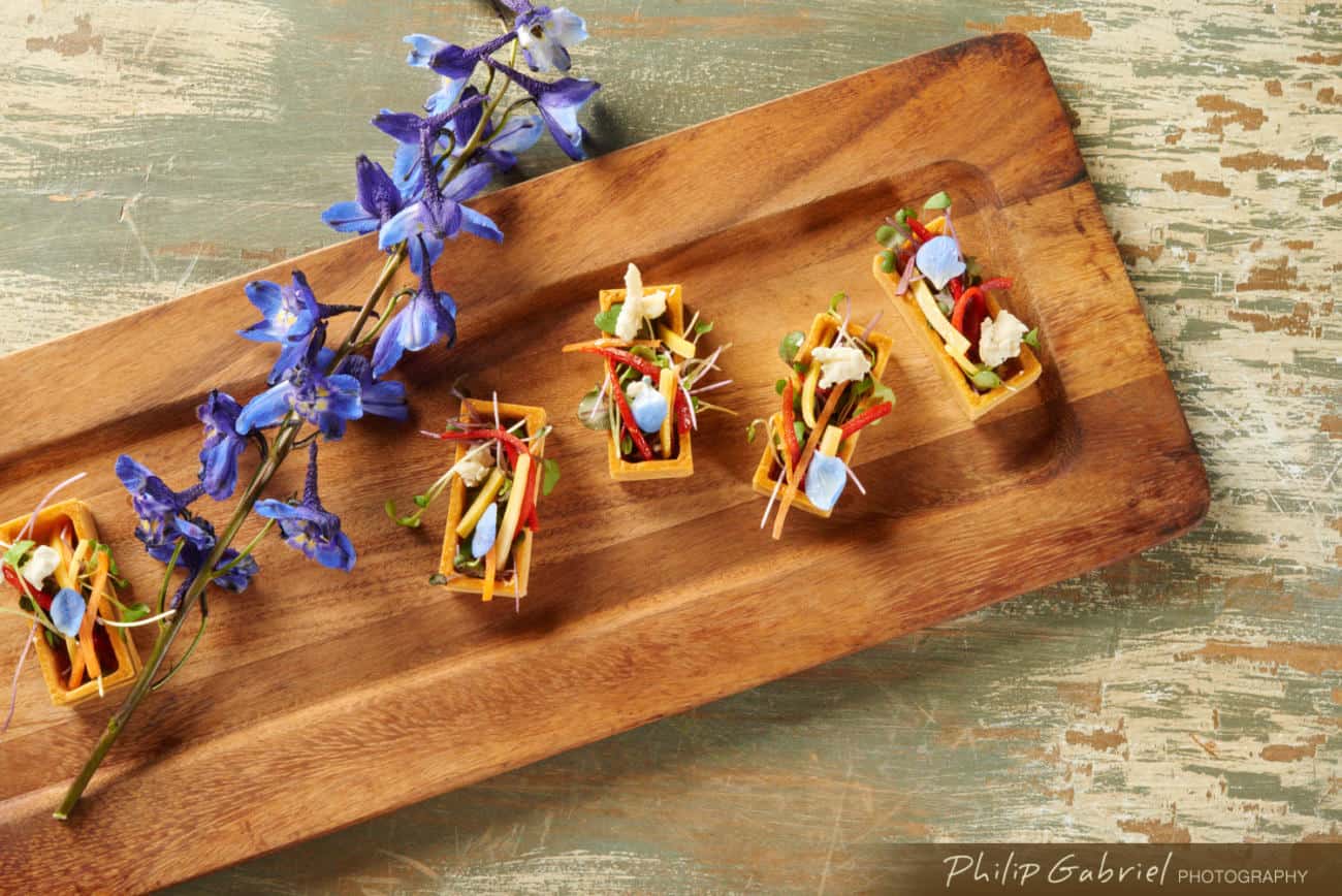 A wooden plank with small-bite appetizers and a colorful blossom