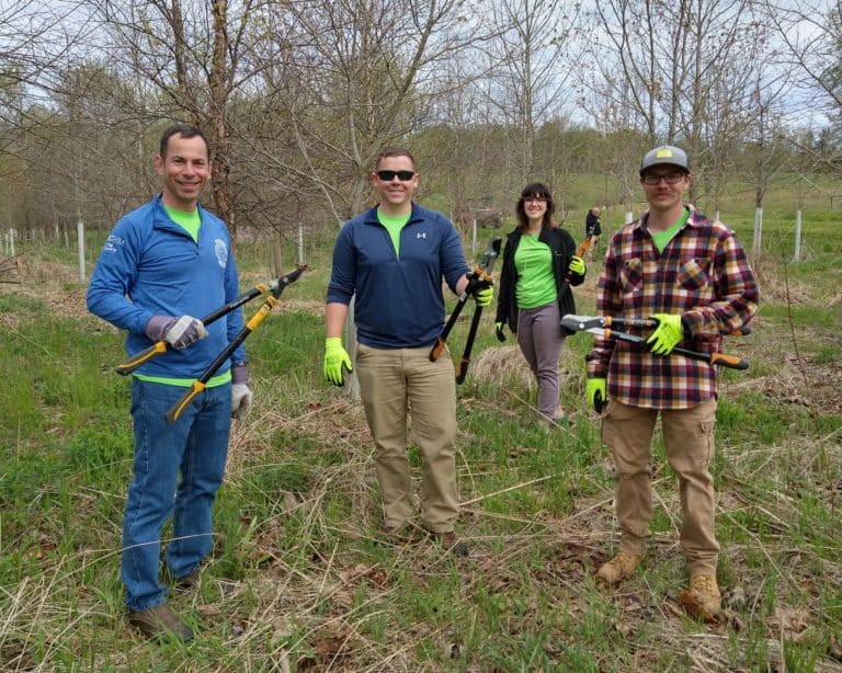 Four people standing in a field holding tools for volunteer service