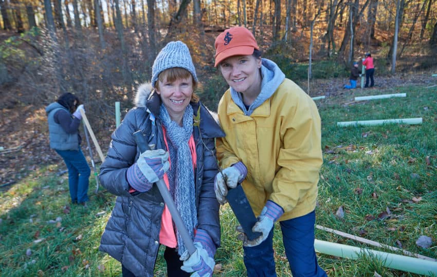 Two volunteers bundled up in a natural setting planting trees.
