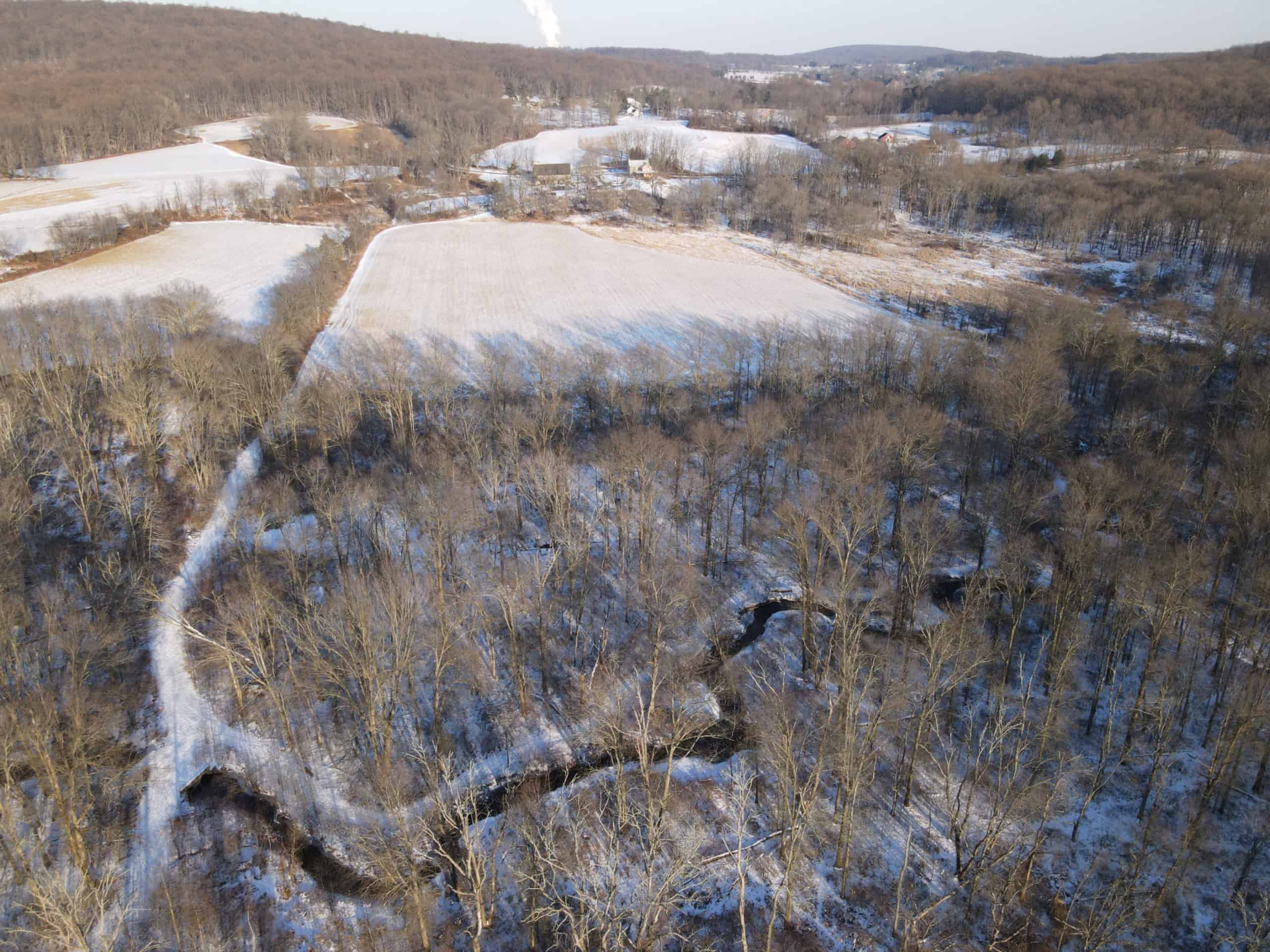 Aerial photo of snowy woods, creek, and fields