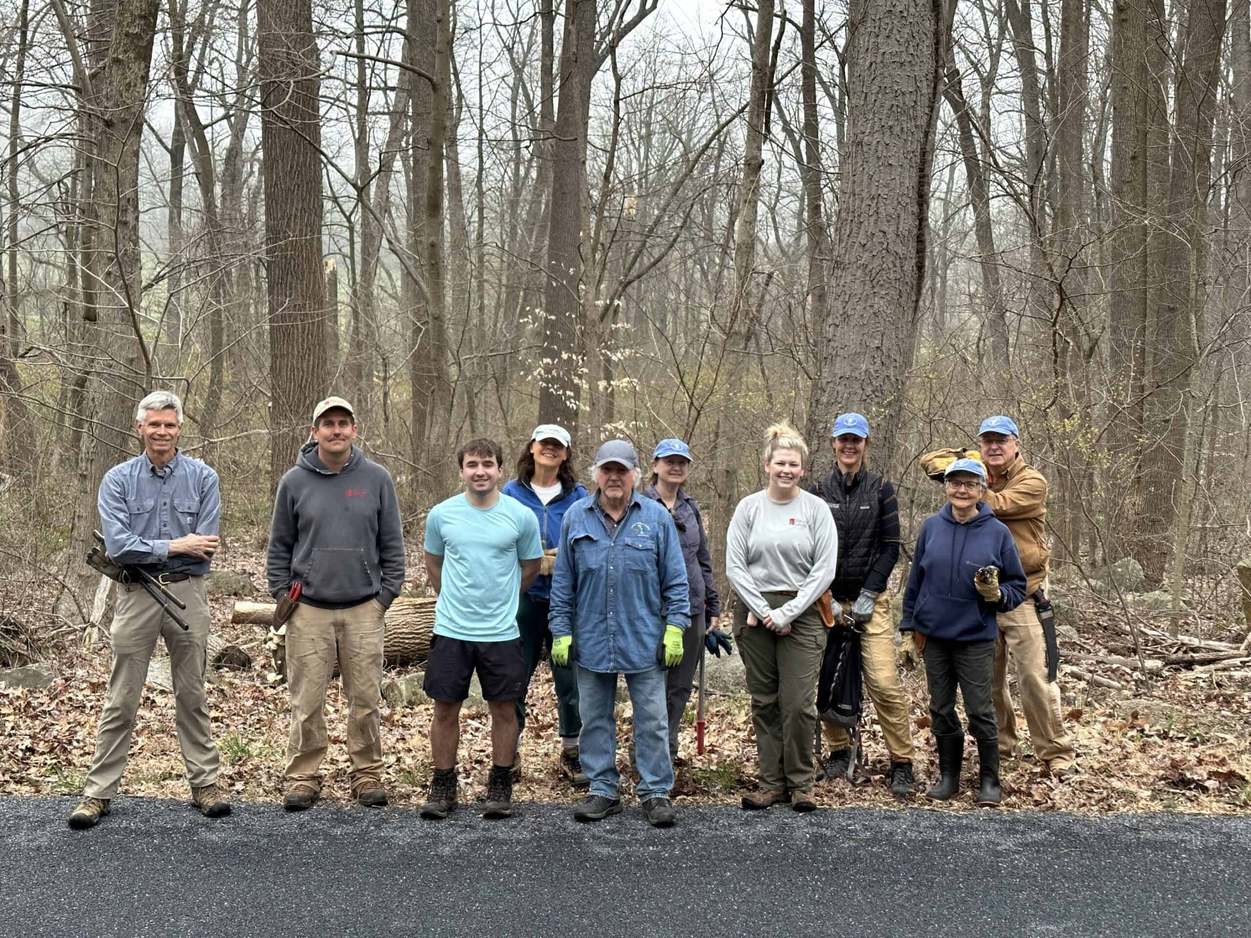 Volunteers posing in front of the woods where they were cutting invasive plants
