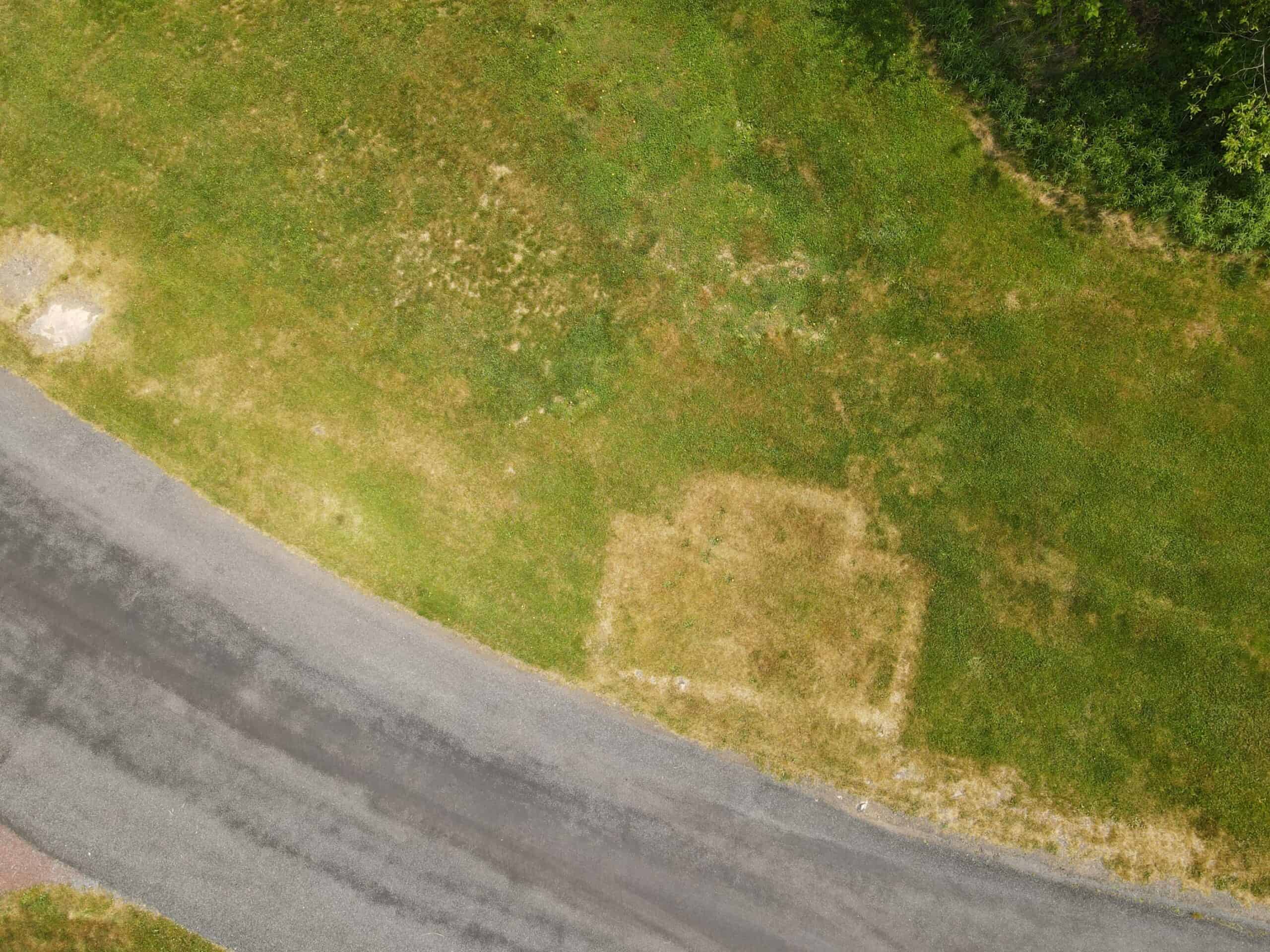 Aerial view of dry turf with outline of a building foundation in dormant grass