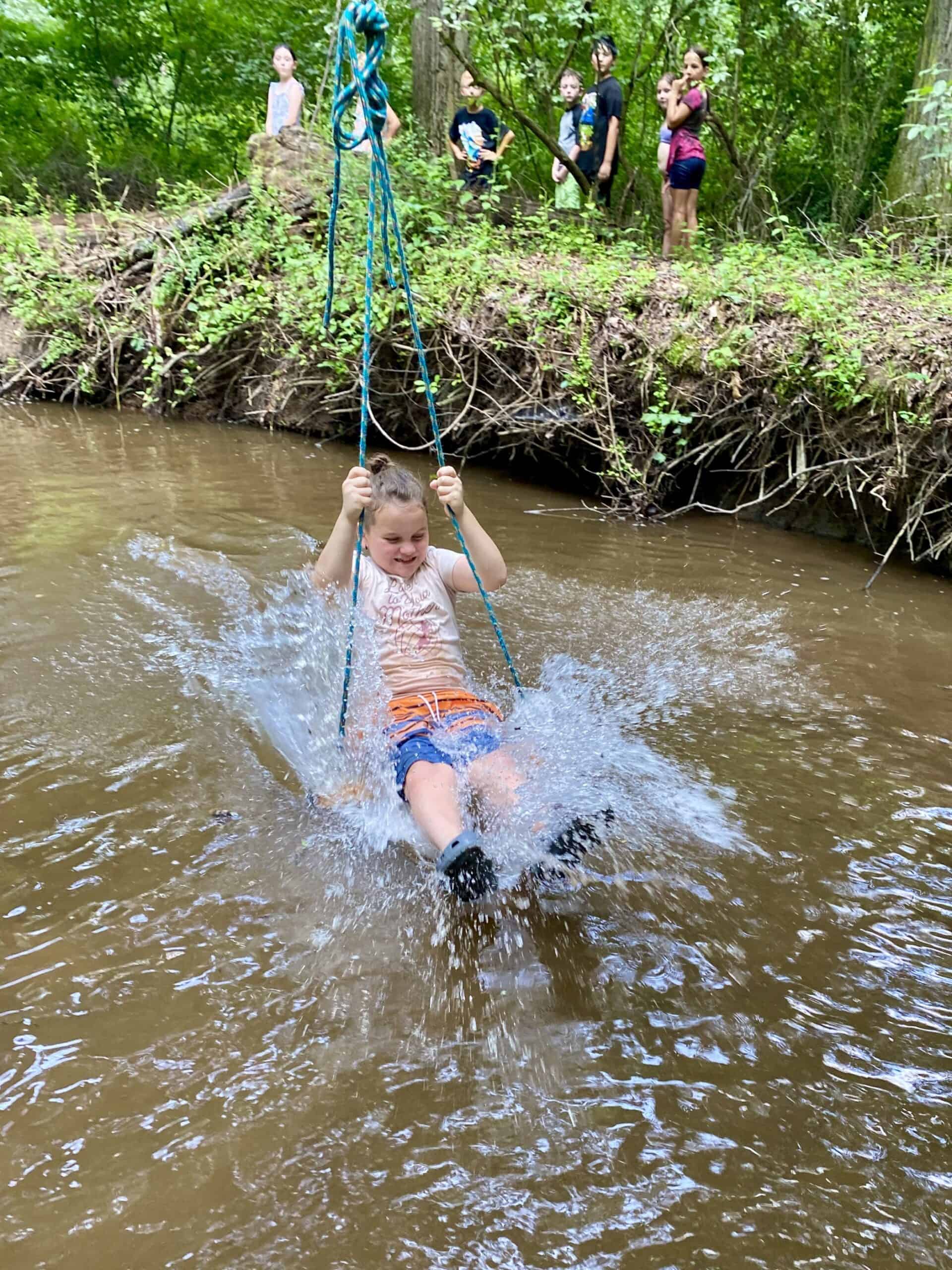 Camper splashing into a creek on a zip line swing