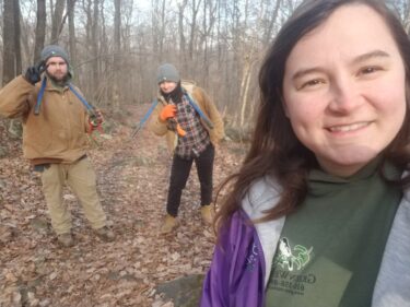 Three workers with tools smile at the camera in a winter woods. 