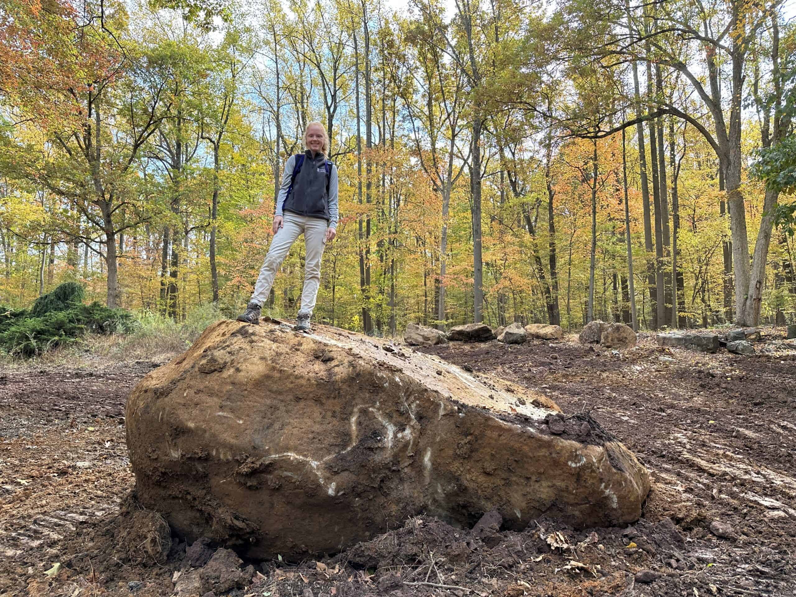 Woman standing on a giant boulder in a clearing in the woods
