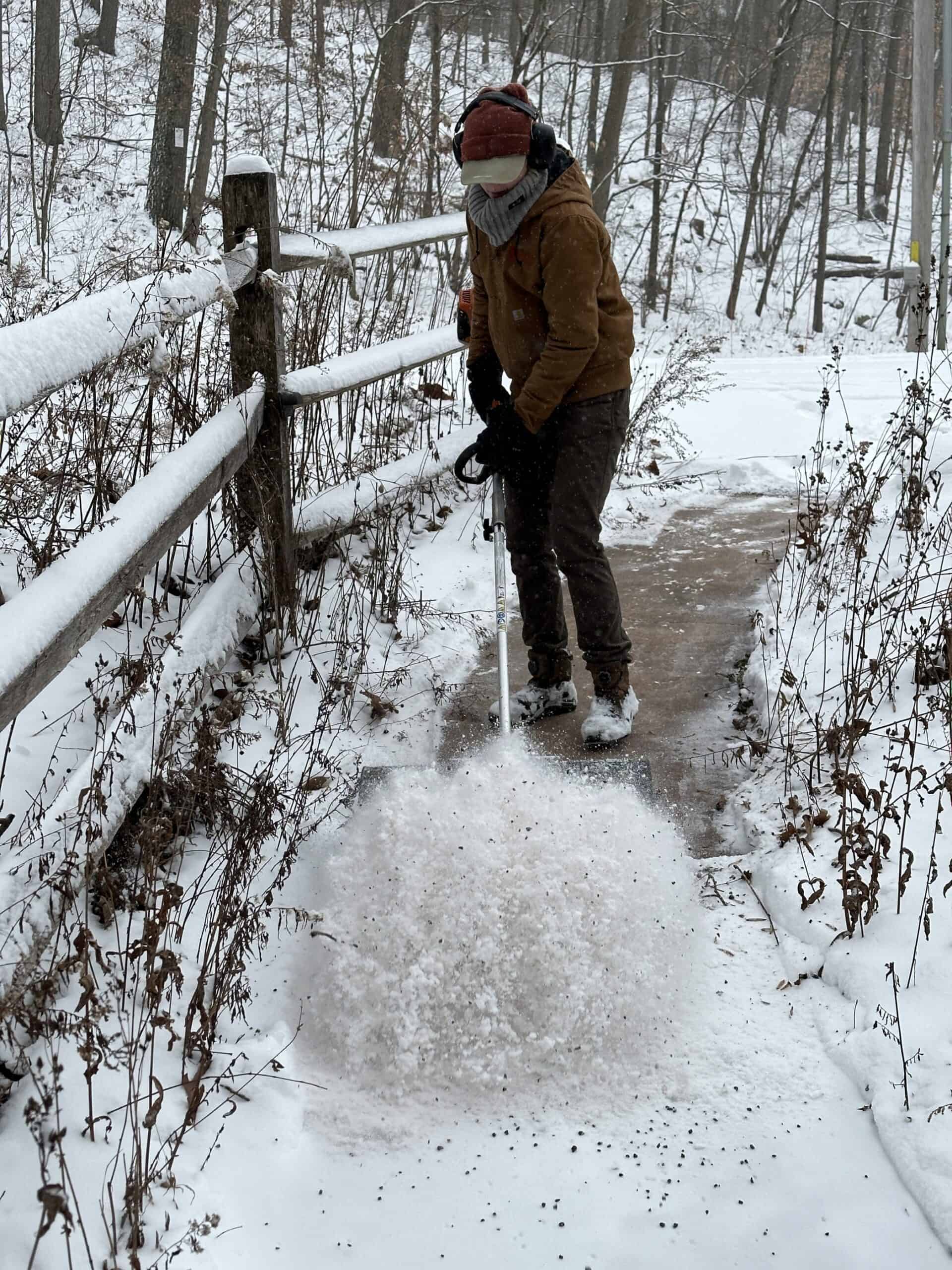 A person using a rotating power brush to clear snow