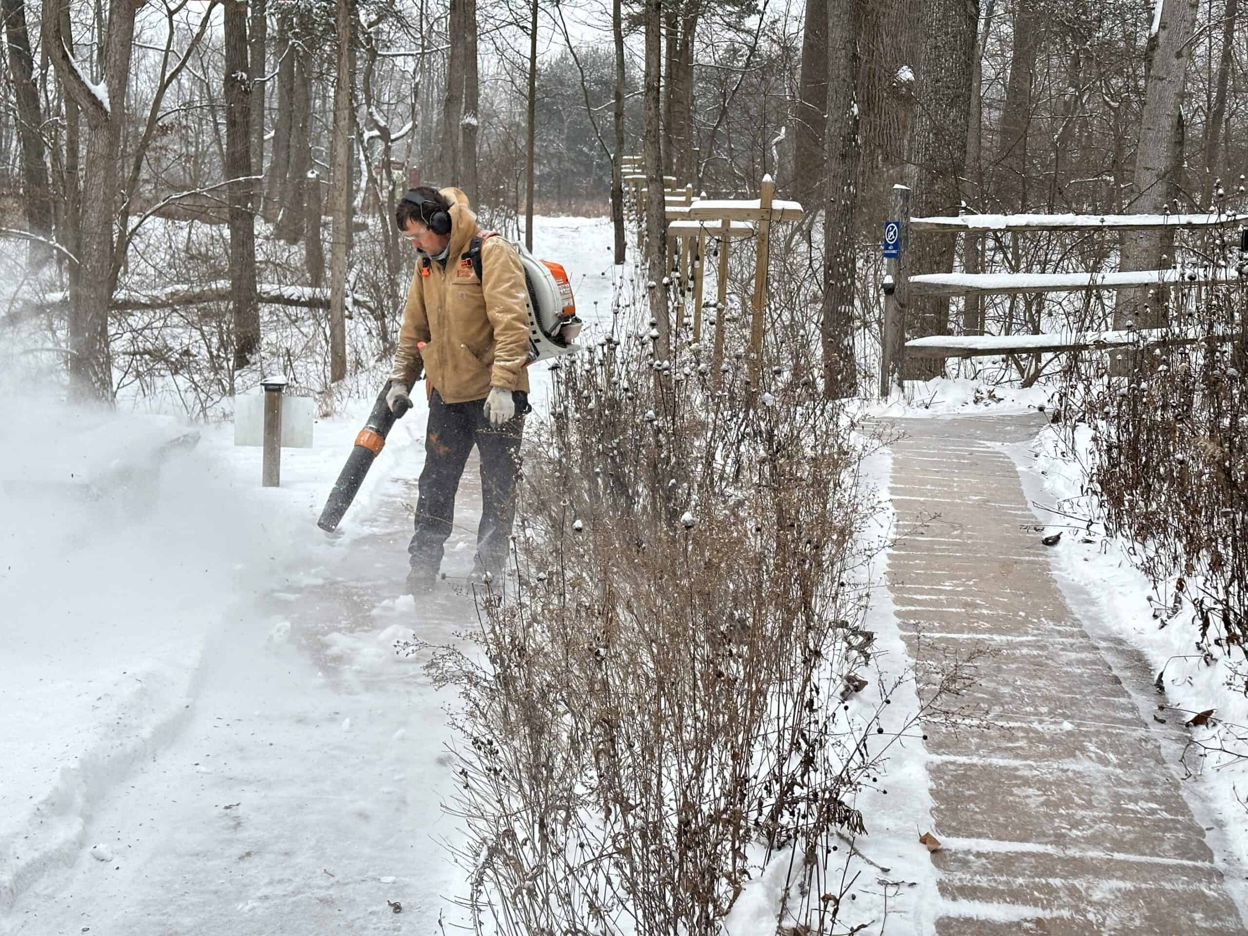 A person using a backpack blower to clear sidewalks