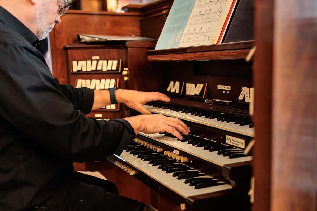 a man with hands resting on a pipe organ keys.