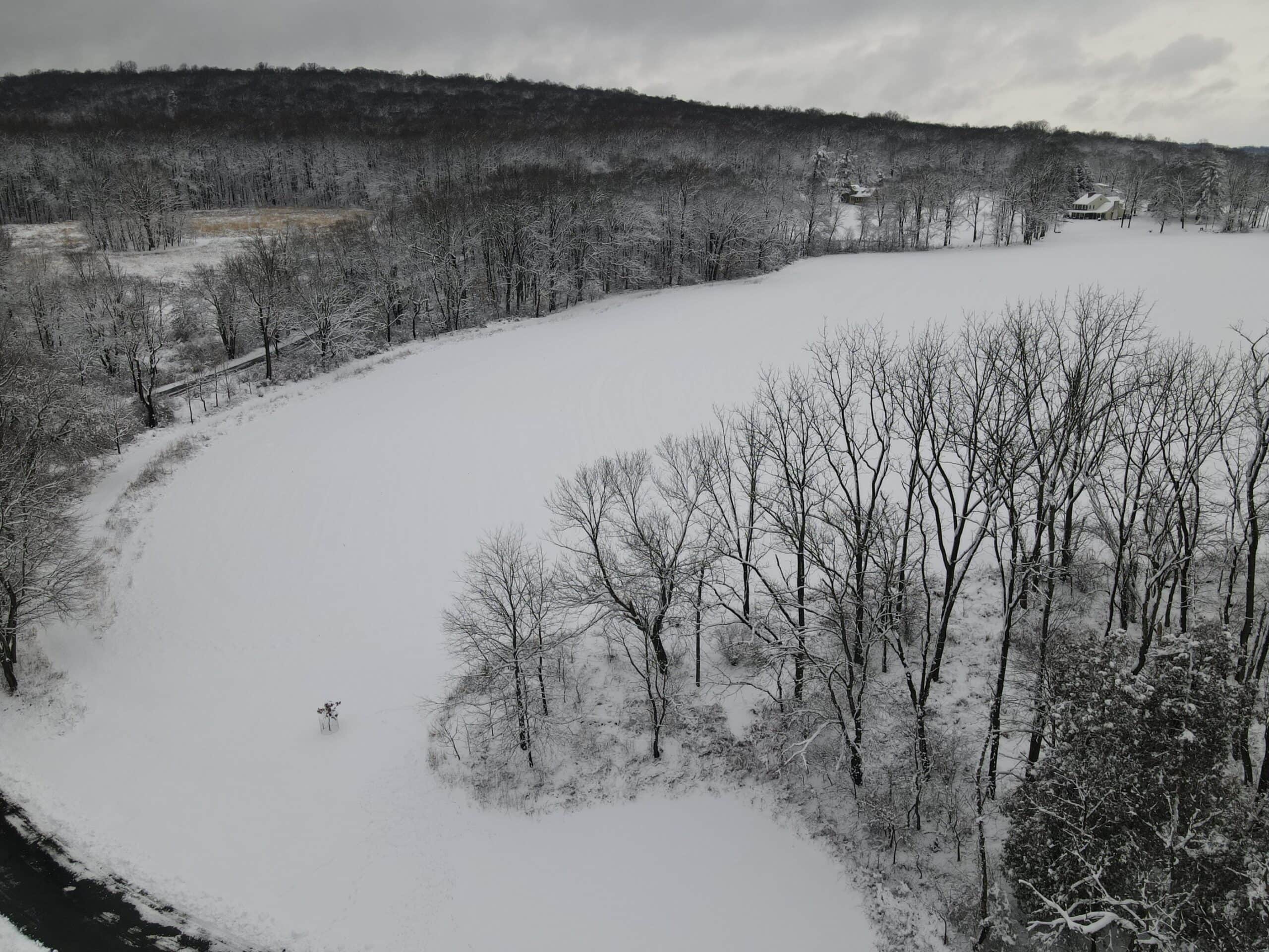 Aerial view of a curving field under snow with forested ridge in the distance
