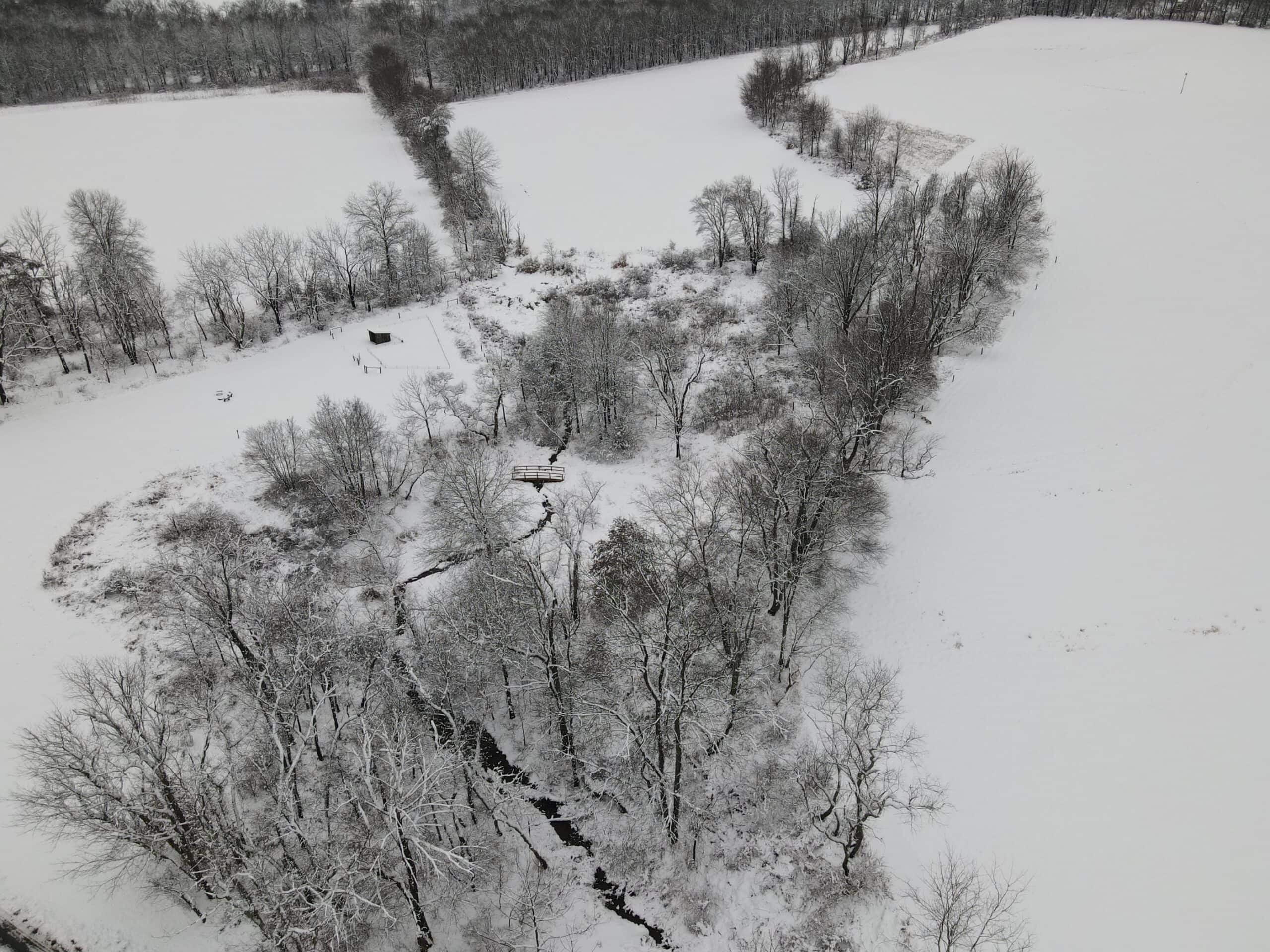 Aerial view of a stream flowing through a wooded valley covered in snow