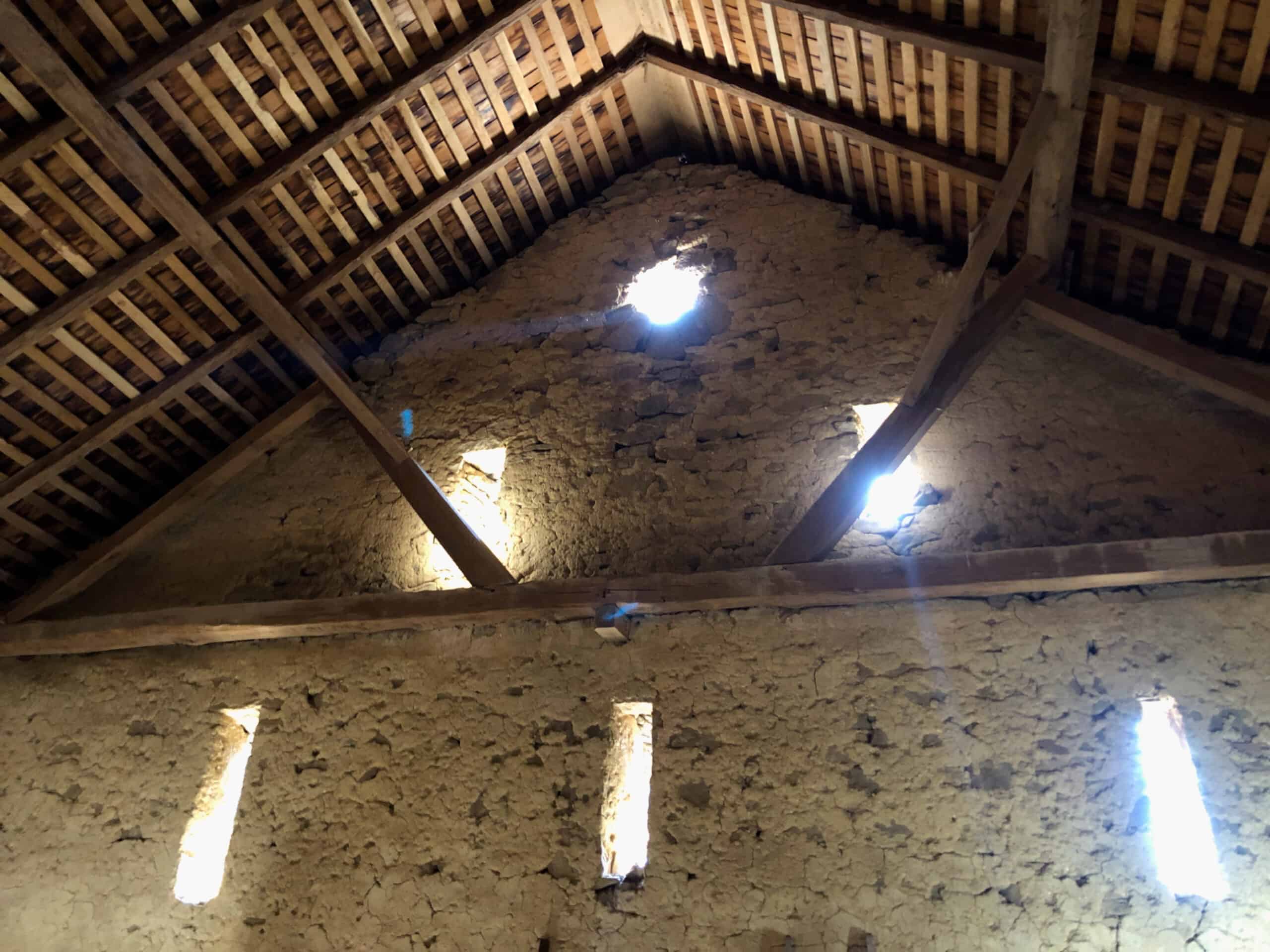 Interior view of historic barn at Crow's Nest Preserve showing queen trusses and ventilation slots in masonry wall.