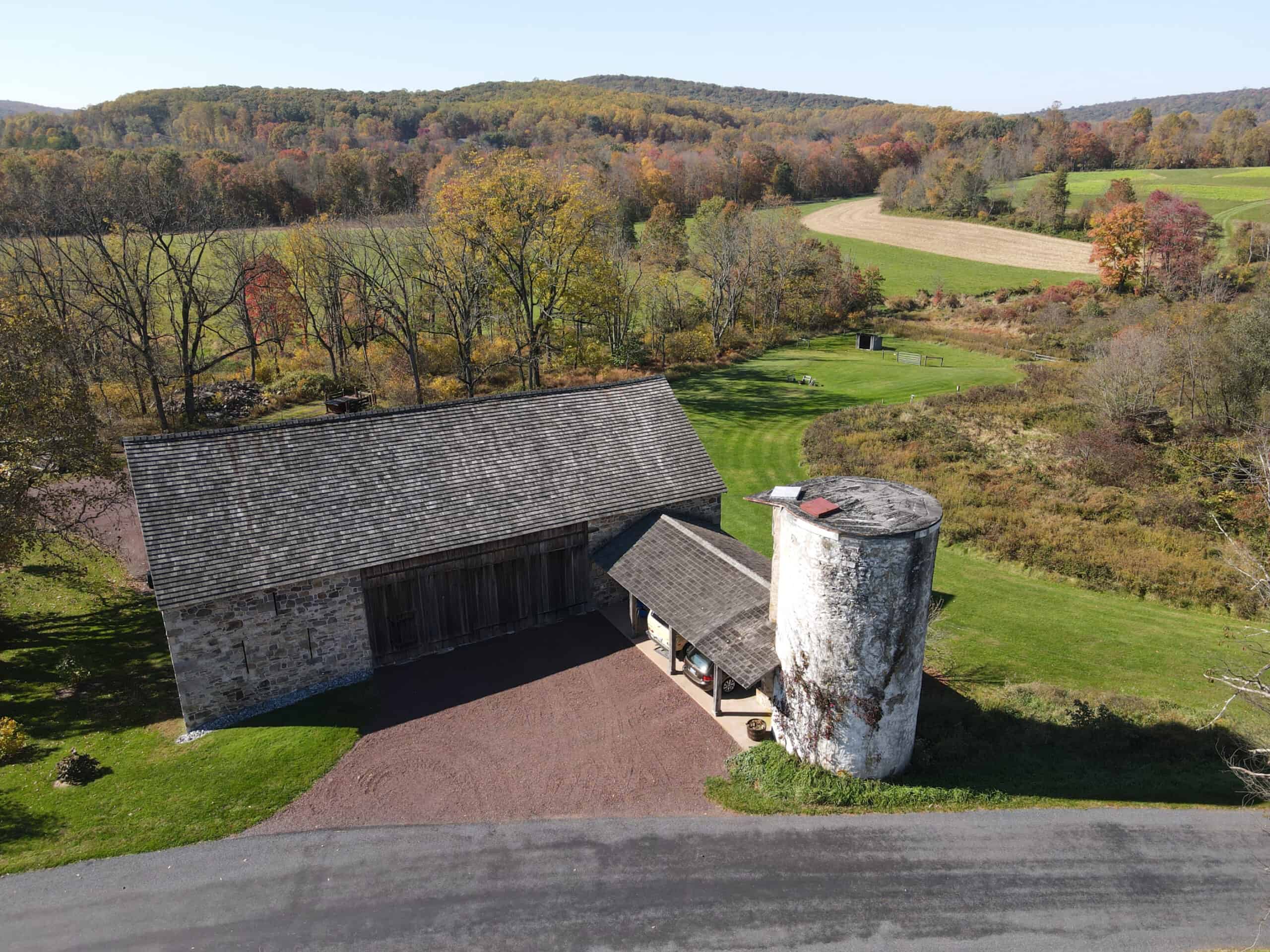 Aerial view of a barn and farm fields and woods beyond.