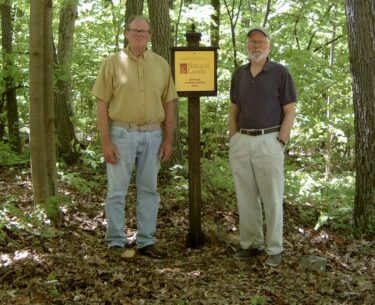 Two men stand in a forest next to a conservation easement sign.