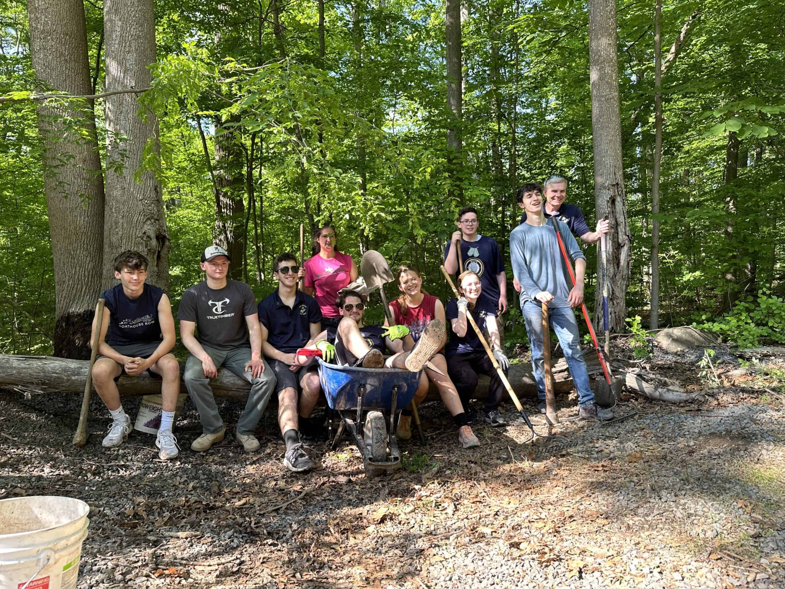 High school students pose with tools after they completed a project in the woods