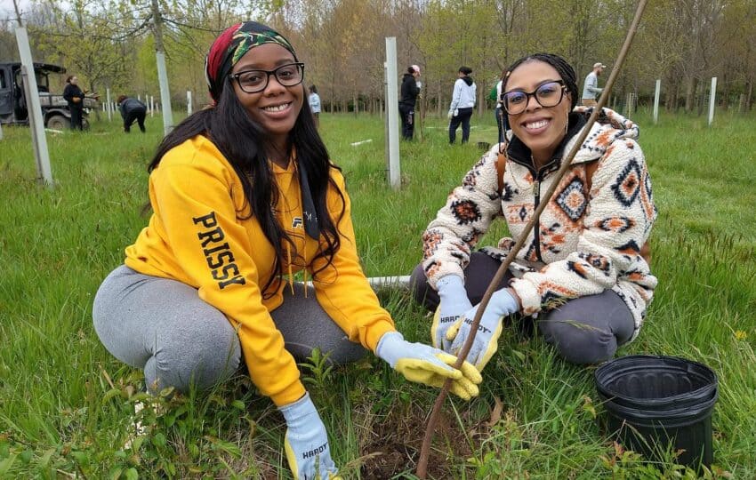 two female volunteers smiling at the camera and planting a tree
