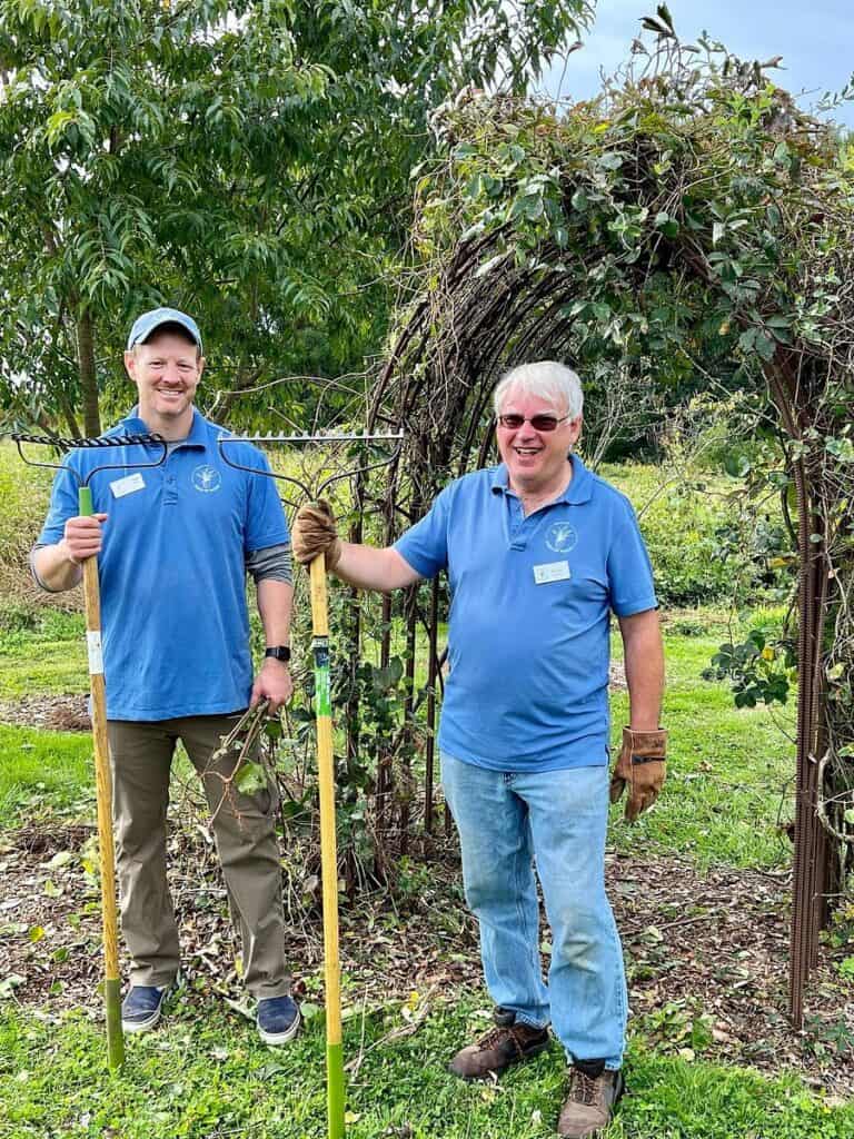 Two men in bright blue shirts smile at the camera holding tools.