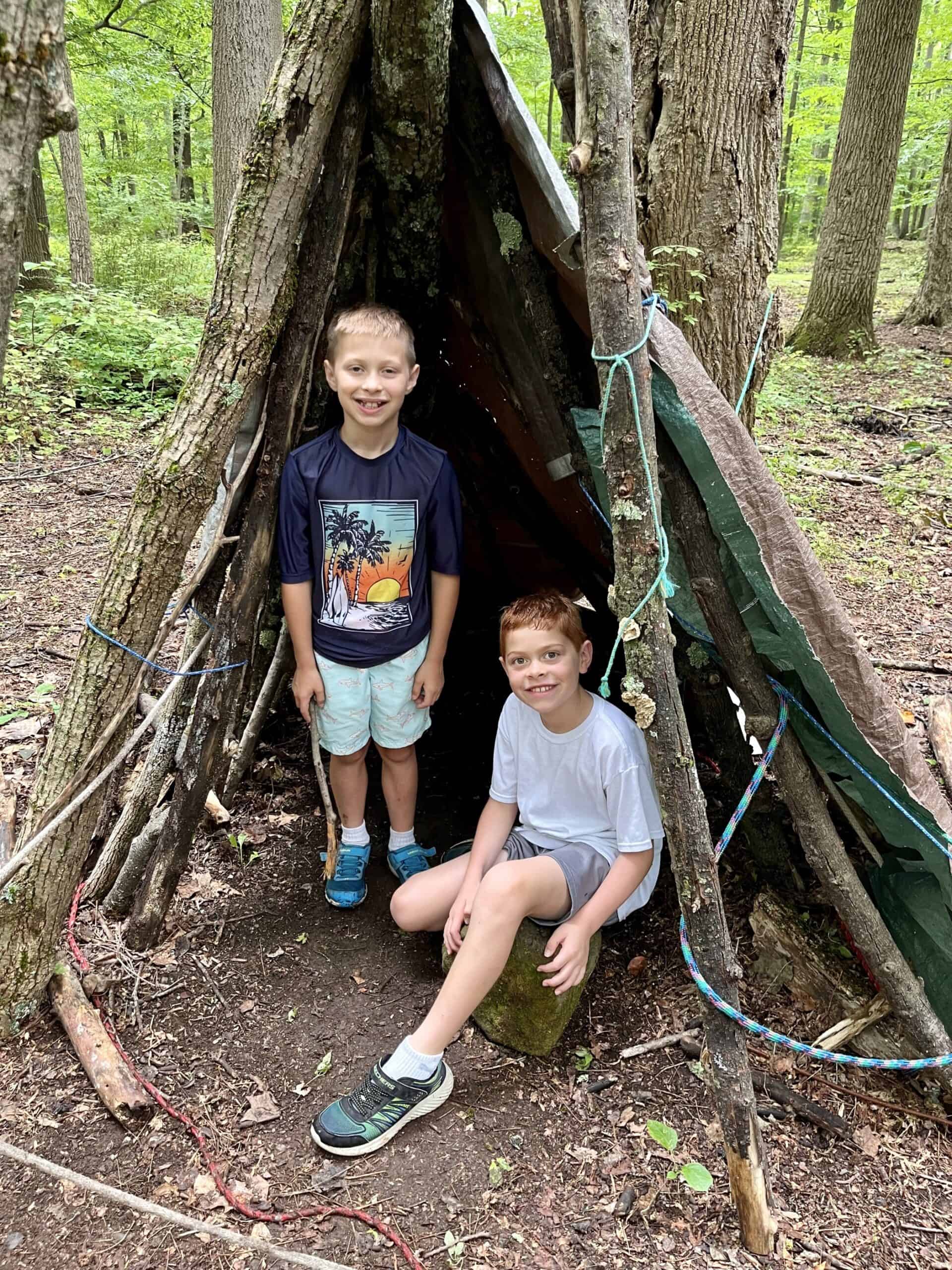 Kids at Crow's Nest camp posing inside a shelter of branches they made