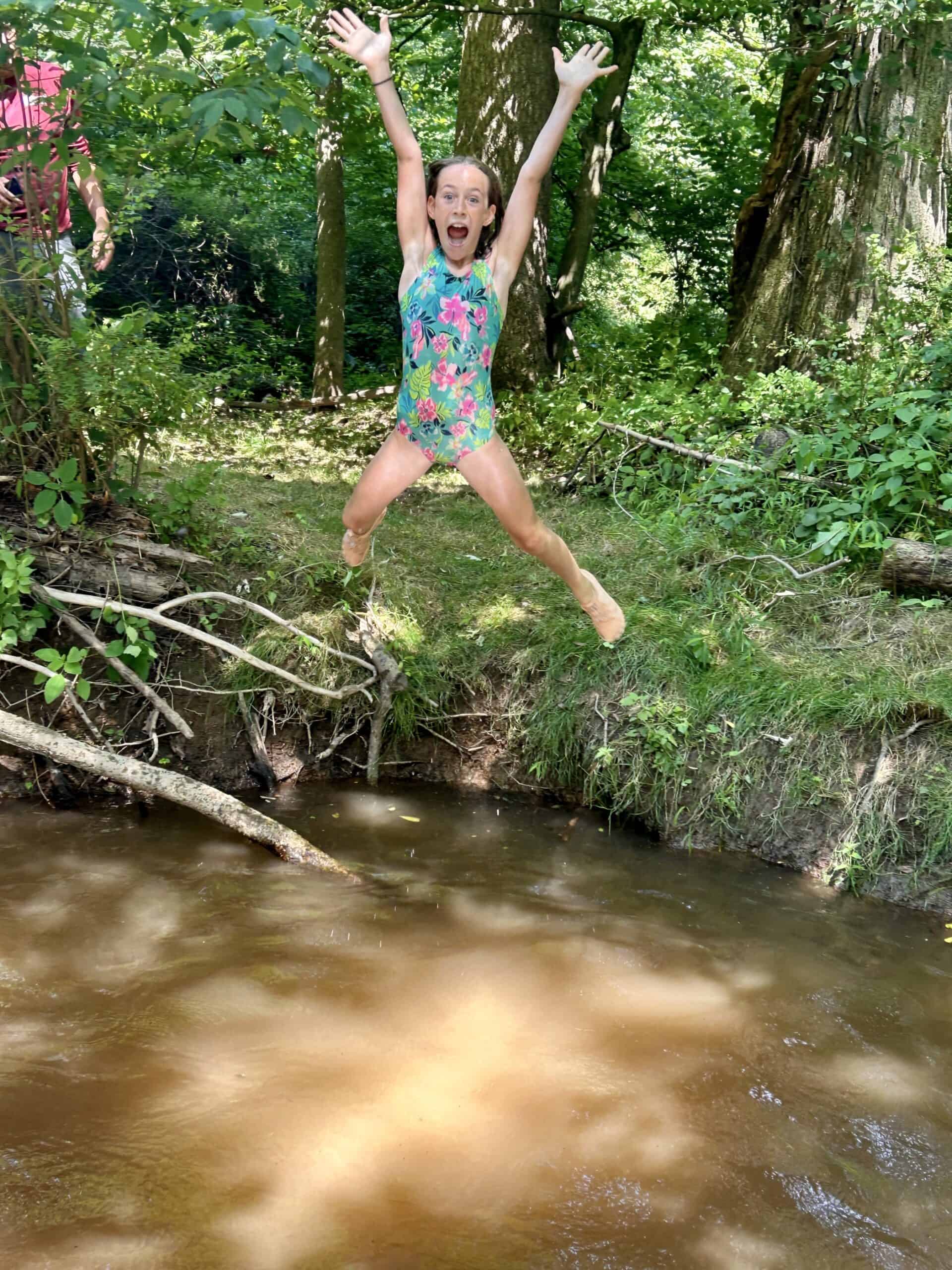 Summer camper leaping into the creek at Crow's Nest Camp.