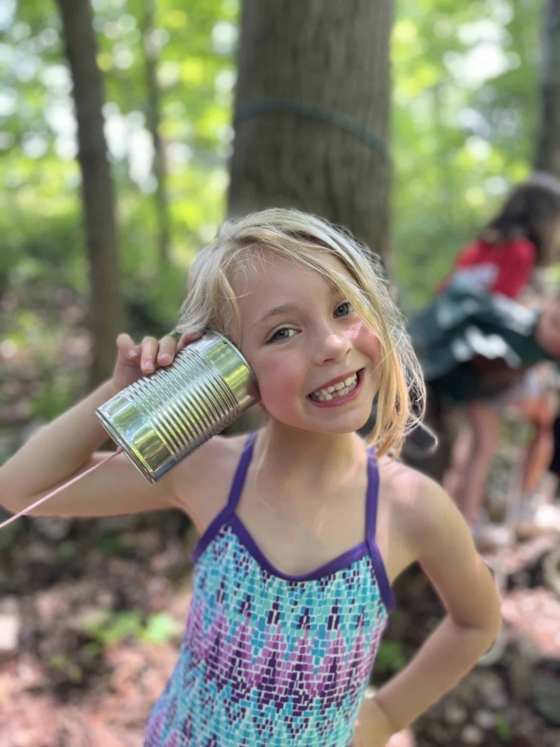 A kid at summer camp listening on a tin-can telephone