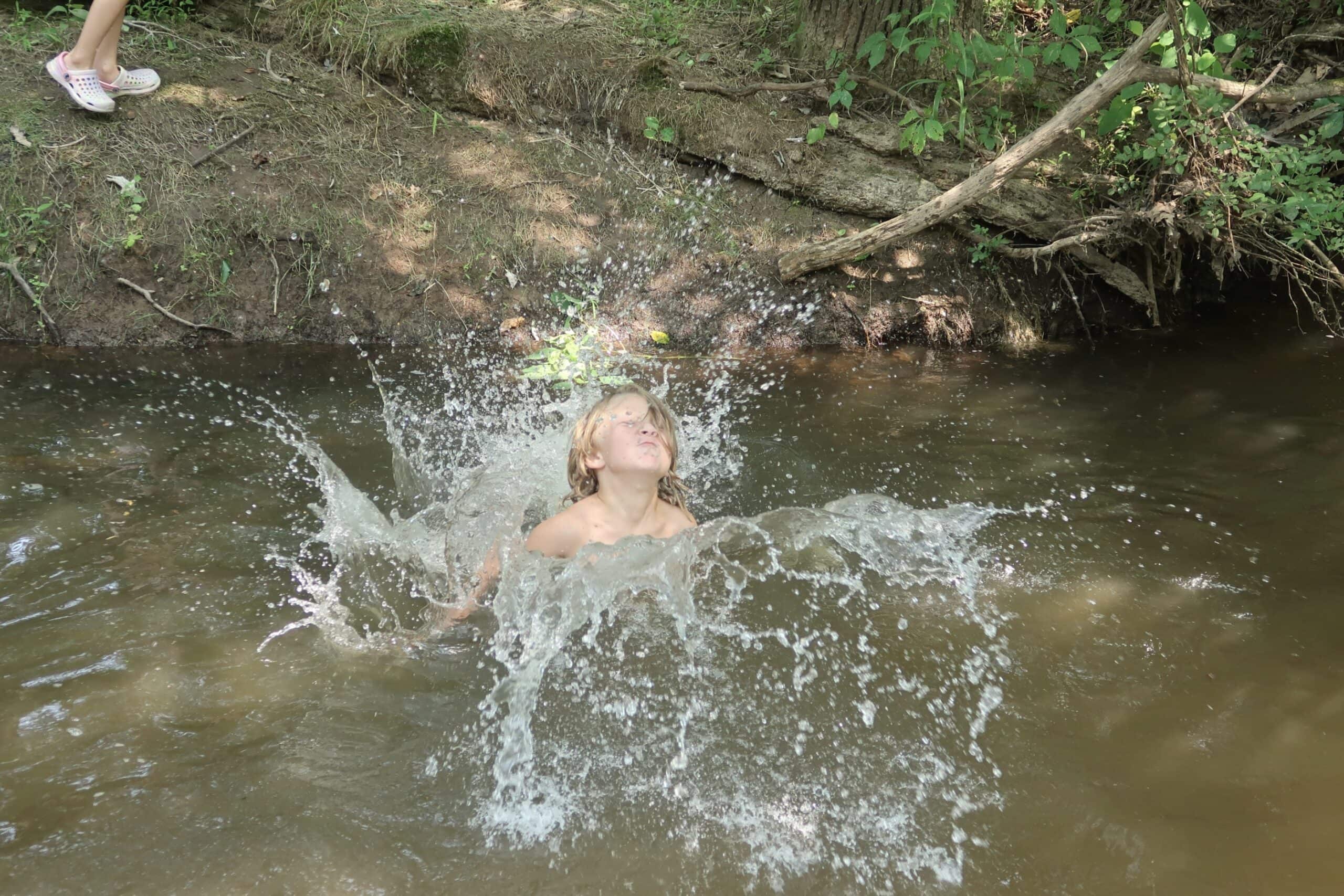 A kid at summer camp landing in the creek with a splash