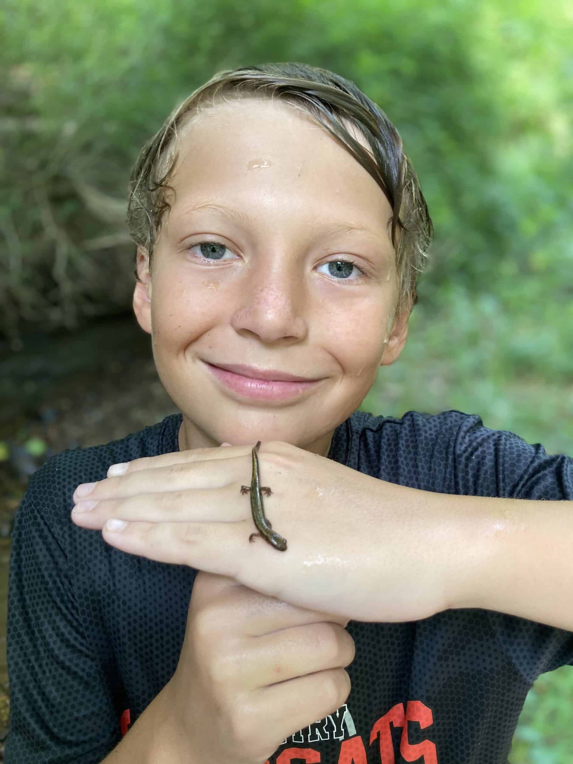 A summer camper holding a salamander on the back of his hand