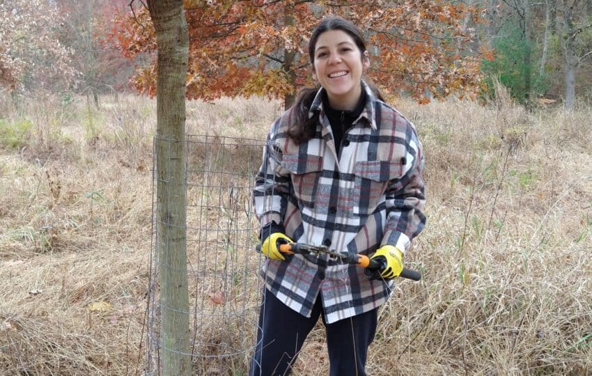 Smiling woman standing next to a tree holding loppers.