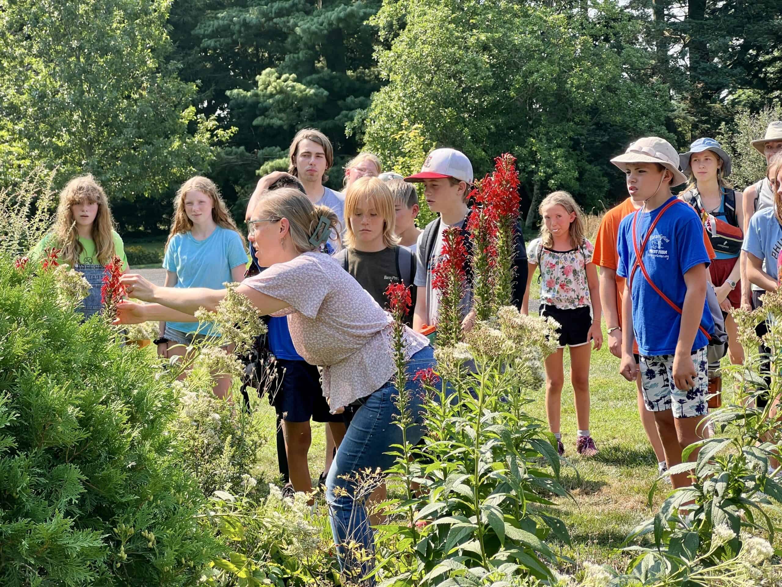 Kids looking at an instructor showing cardinal flower in a garden