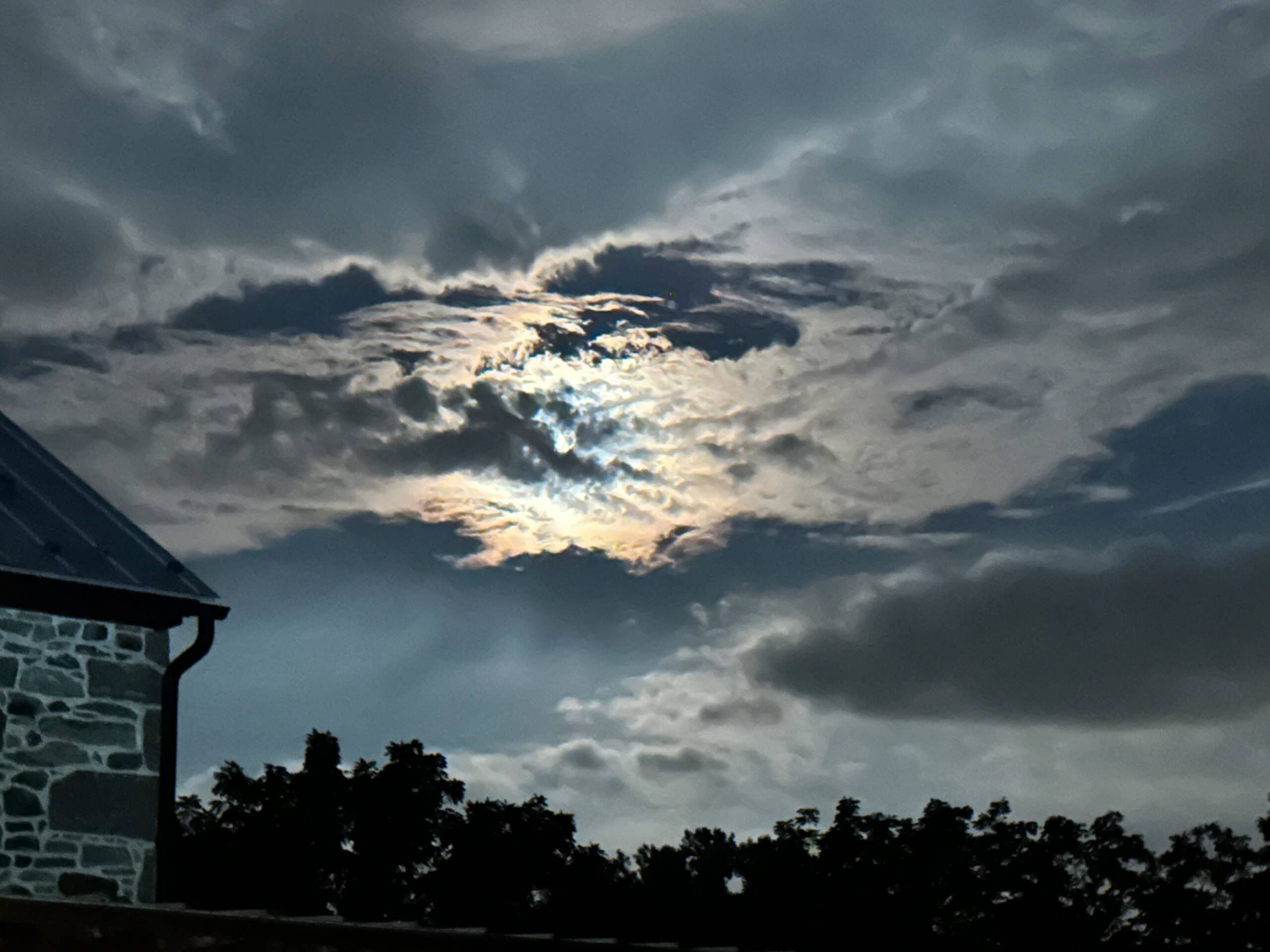 The moon behind the clouds in a spooky image.