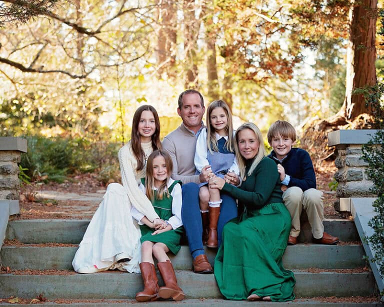 A family of six smiles at the camera on the stone steps at Stoneleign in autumn.