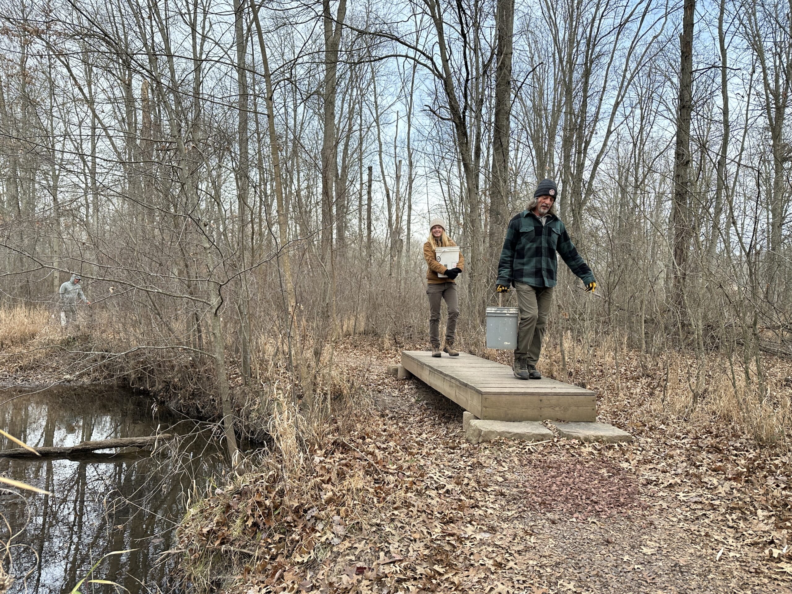 Volunteers hauling buckets of gravel along a trail.