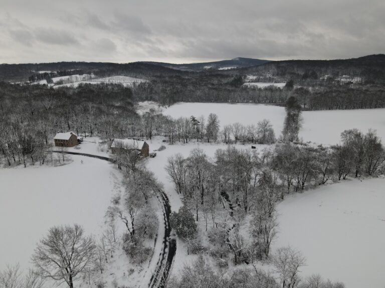 Aerial photo of fields, hedgerows, woods, barn, farmhouse in the snow on an overcast day