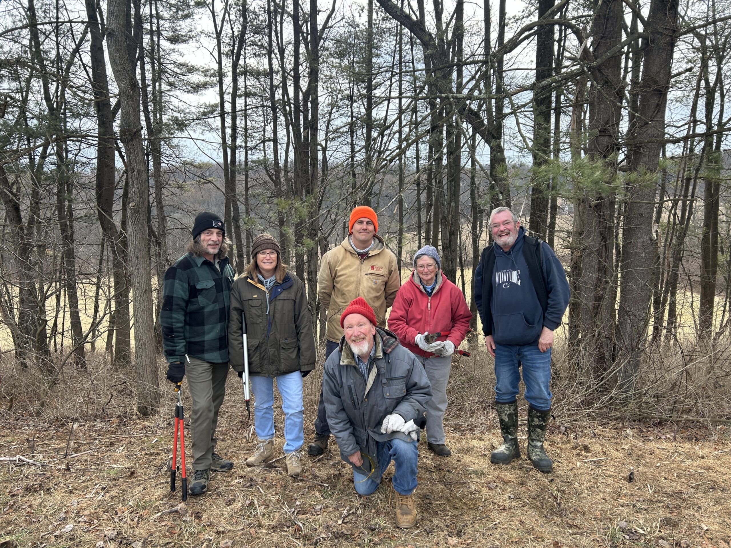 Volunteers posing in front of the woods they are taking care of.